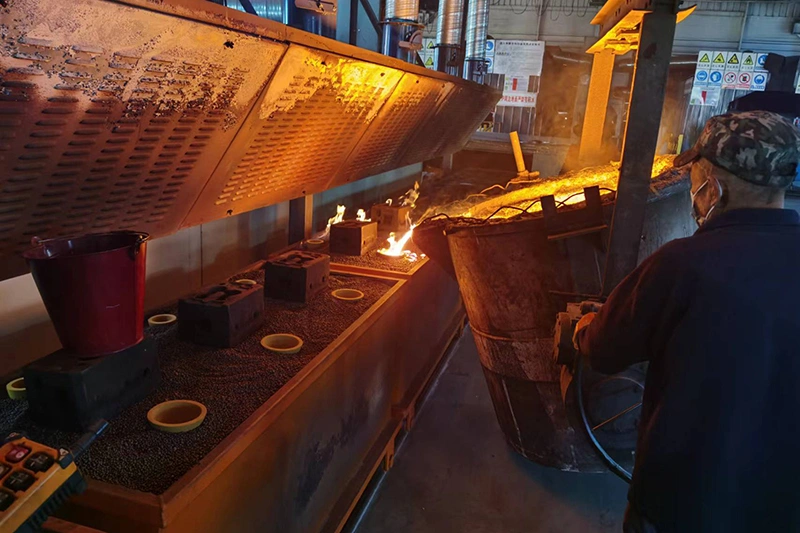 A man operates a large furnace in a factory, surrounded by metal castings and industrial equipment
