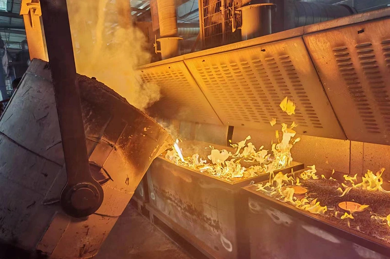 A metal furnace filled with fire and smoke, used for sand casting processes in metalworking
