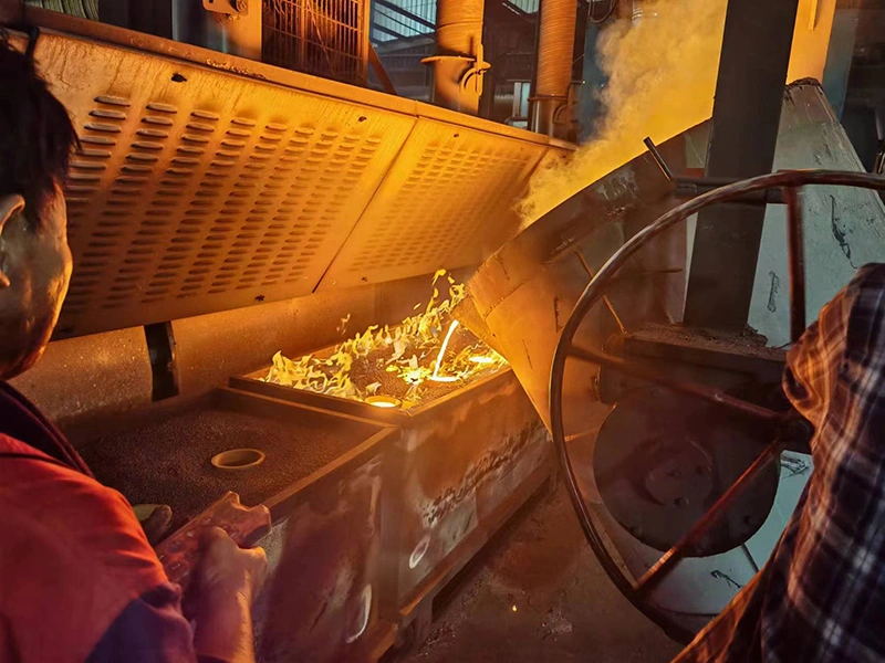 Two men work in a factory, engaged in sand casting, with a fire visible in the background